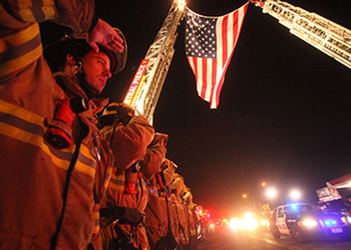 Pierce County firefighters salute while an American flag waves over the street.